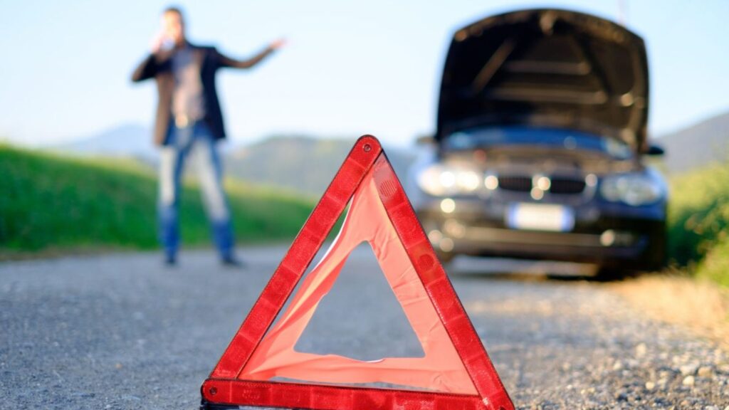 A man standing beside a car with a broken hood, experiencing a car breakdowns